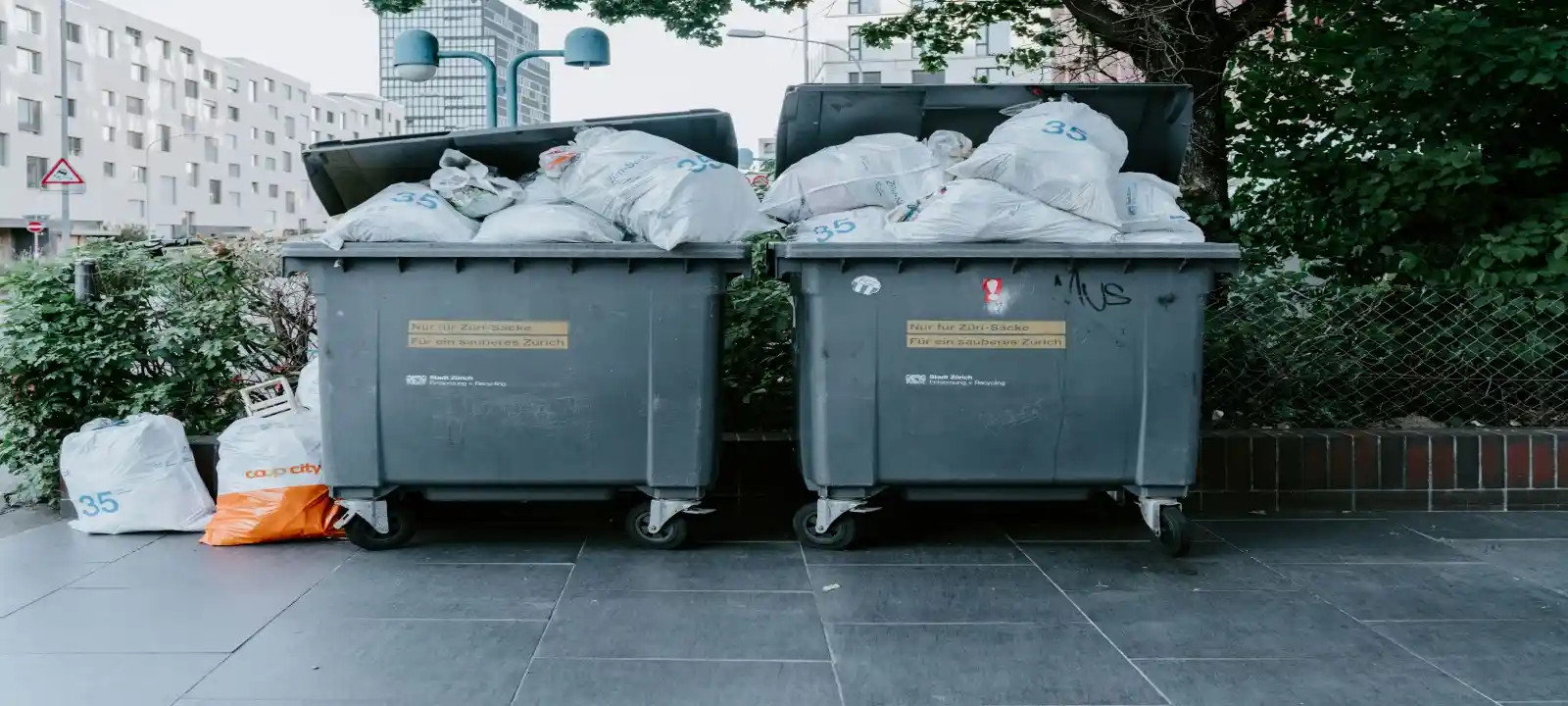 Two large skip bins filled to the brim, with several bags of rubbish placed beside them, for cheap skip bins wollongong.
